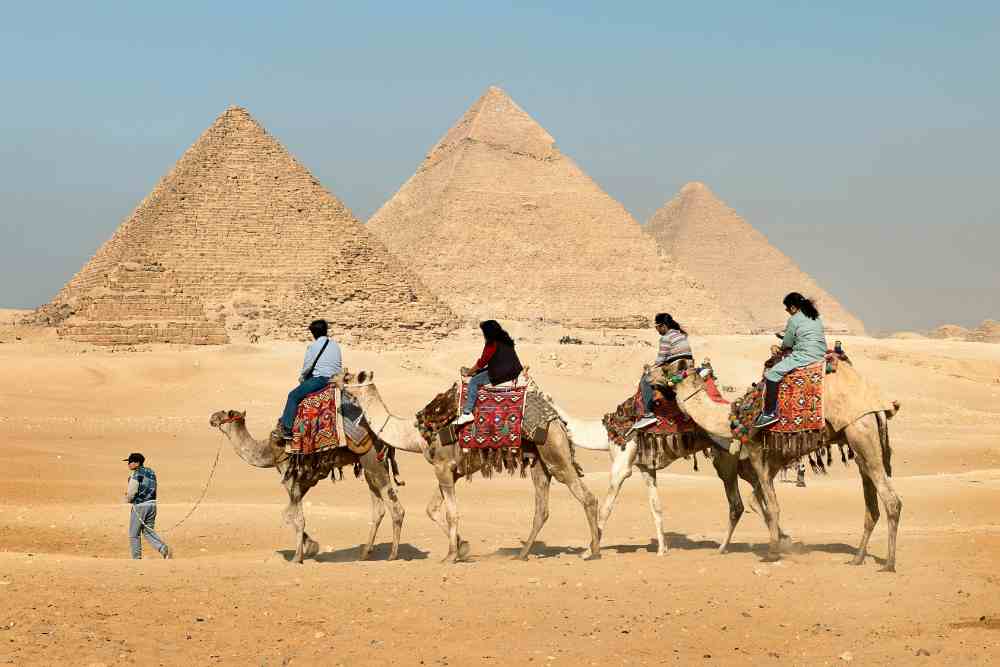 Four People Riding on Camels Across the Pyramids, Giza Governorate, Mısır