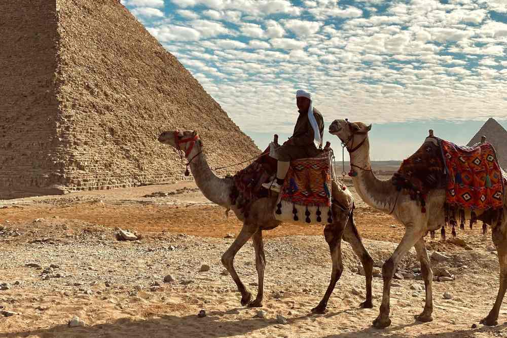 Two people riding camels in front of the pyramids